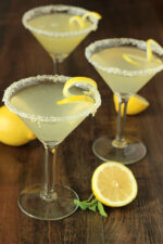 Three stunning lemon drop martinis with twists and sugared rooms. The table is decorated with a few lemons.