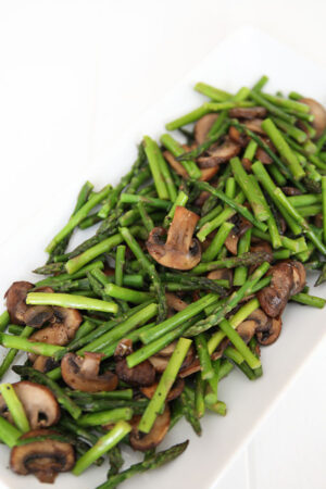 A beautiful white platter with tender spears of sauteed asparagus and caramelized slices of mushrooms