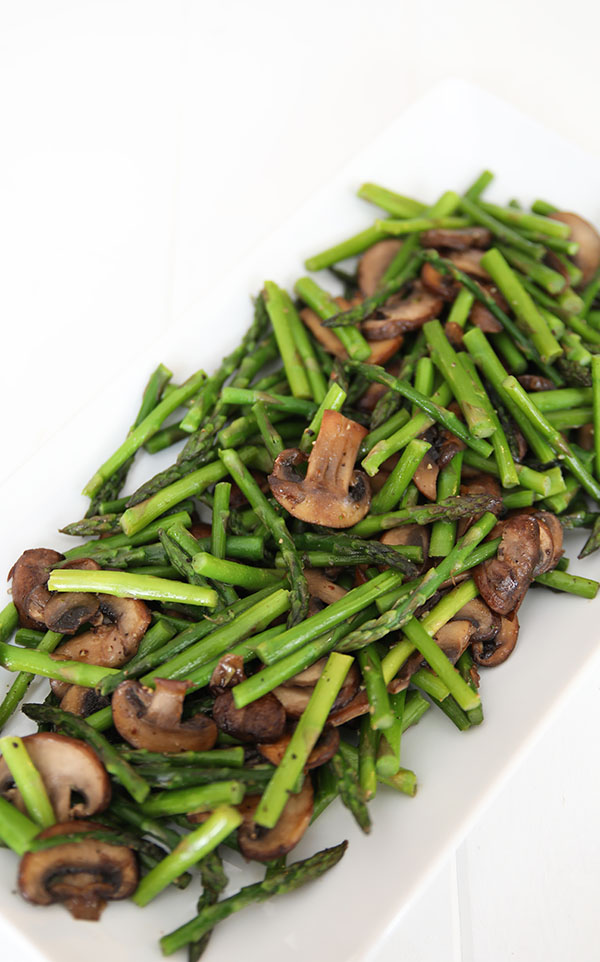 A beautiful white platter with tender spears of sauteed asparagus and caramelized slices of mushrooms