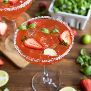 Sweet and juicy fresh strawberry margaritas on the rocks with limes and basil microgreens.