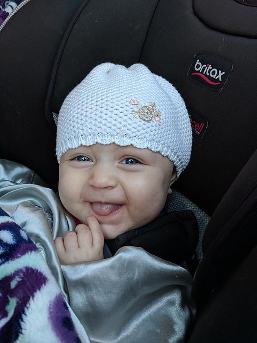 Baby Ella in a white knit hat smiling at the camera.