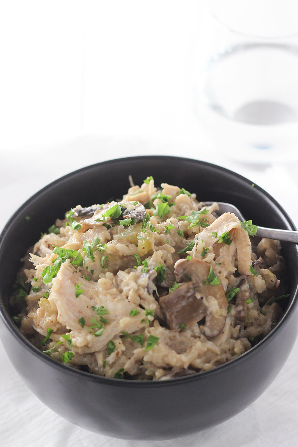 A black bowl is full of creamy instant pot chicken and rice. You can see slices of mushrooms and shredded chicken.