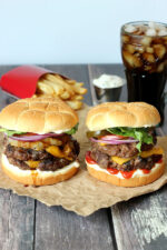 Two stunning burgers with melted cheese, condiments, fries and a coke.