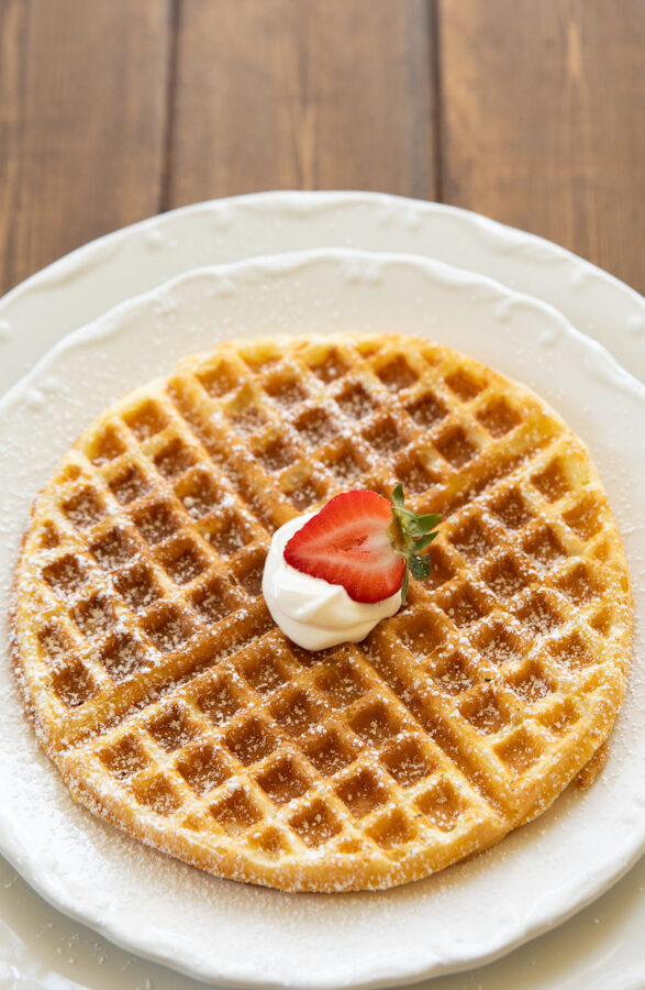  This buttermilk waffle is topped with a dollop of sour cream and a dusting of powdered sugar and garnished with half a strawberry.