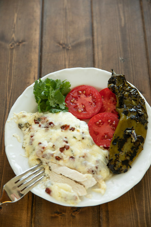 A plate of dinner features a big serving of hatch chile chicken bake, some sliced tomatoes and a whole roasted hatch chile.