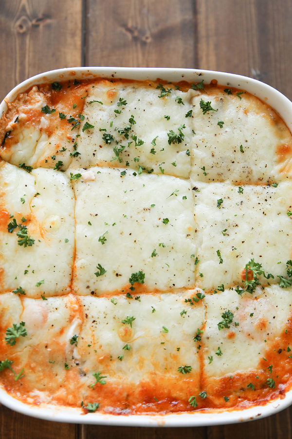 A square white baking dish is full of hot, keto zucchini lasagna. There is lots of mozzarella cheese and a little parsley on top.