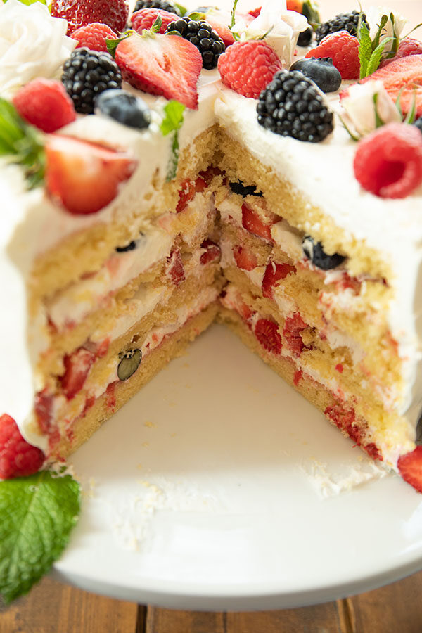 Easy Berry Chantilly Cake with a big wedge out.  Here you can see the layers of whipped cream, jam, and fresh berries.