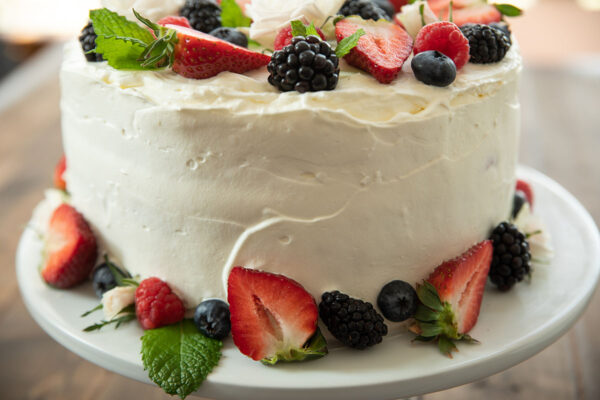 A close up of the side of a Berry  Chantilly Cake.  The frosting is spread on but not perfectly smooth.  Fresh berries make it beautiful.