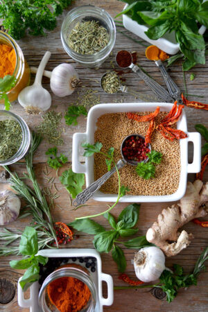 The wooden table is covered in bulbs of garlic, dried herbs and fresh herbs.