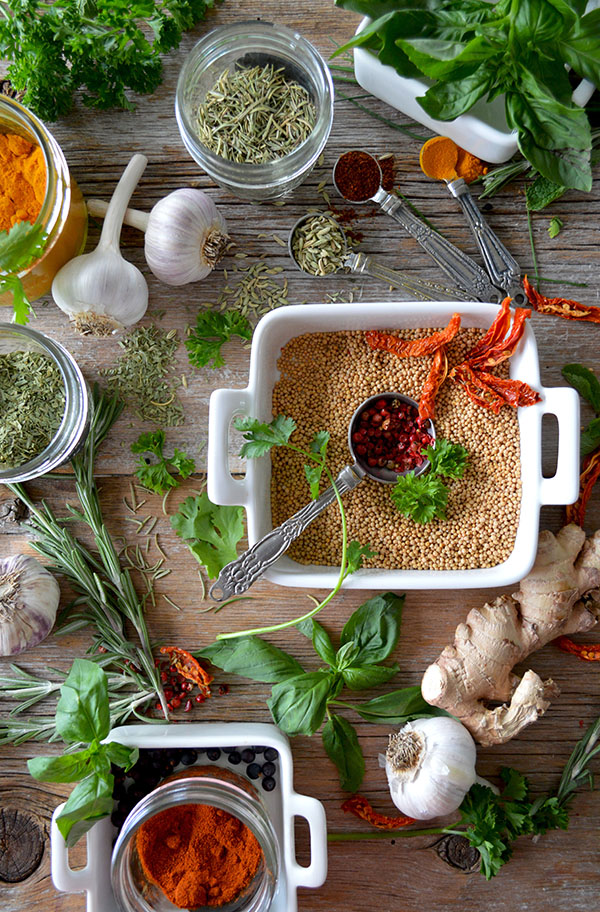 The wooden table is covered in bulbs of garlic, dried herbs and fresh herbs.