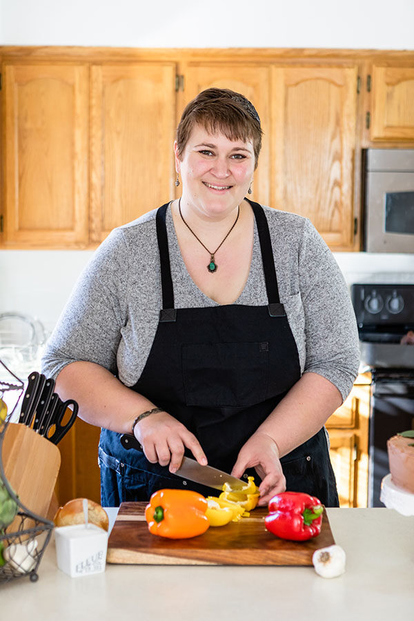 Mirlandra stands at a counter slicing bell peppers on a wooden cutting board. 