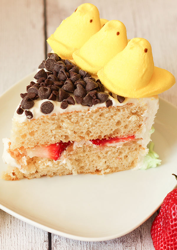 A slice of peeps sunflower cake. The cake is two layers of yellow cake with strawberries in the middle. The top is decorated with chocolate chips and peeps.