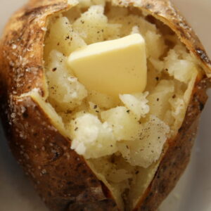 This is a perfectly baked potato that is crispy on the outside and fluffy on the inside. The skin is crusted with salt and a pat of butter is melting on the potato.