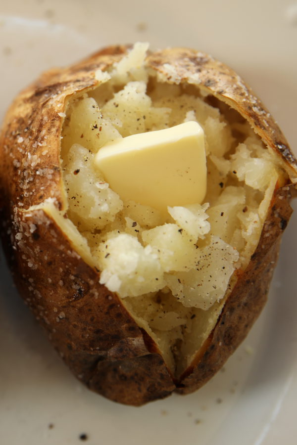 This is a perfectly baked potato that is crispy on the outside and fluffy on the inside. The skin is crusted with salt and a pat of butter is melting on the potato.