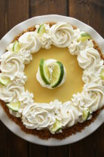 an authentic key lime pie in graham cracker crust. The whipped cream is swirled on and wedges of lime garnish the pie.