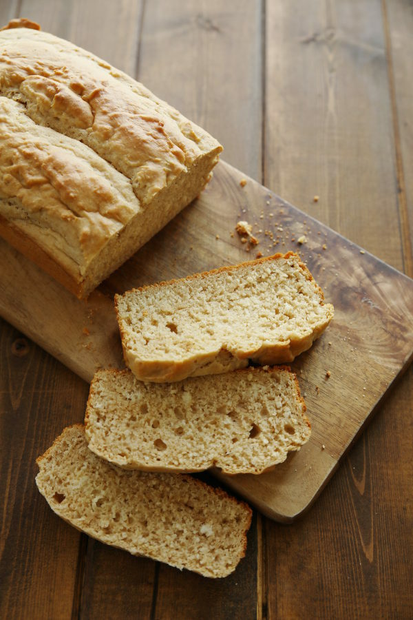 A loaf of peanut butter quick bread sits on a cutting board. Three slices are set out ready for nibbling.
