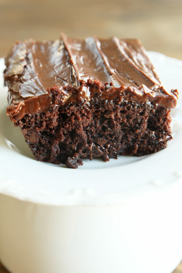 A slice of wacky cake. This is a square of chocolate cake with frosting on a white plate.