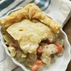 a slice of ham and chicken pot pie in a white dish. The dish is sitting on a white and blue stripped dish towel on a wooden table.