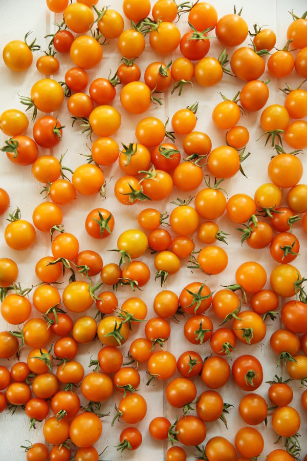 Sungold cherry tomatoes sit on a white wooden table ready to be frozen.