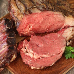 A big prime rib roast is resting on a cutting board. One slice has been cut off and sits face down ready to serve.