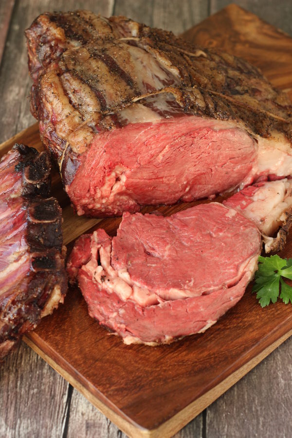 A big prime rib roast is resting on a cutting board. One slice has been cut off and sits face down ready to serve.