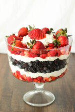 A large glass pedistil dish is layered with strawberries, raspberries, blueberries, blackberries and whipped cream for a pretty patriotic fruit saladi.