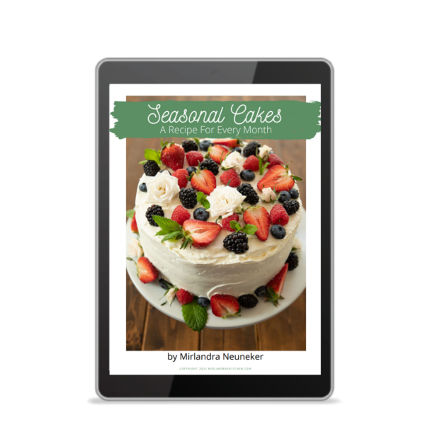 A cover image of the Seasonal Cakes Cookbook features a lovely fruit and flower covered layer cake with buttercream frosting.