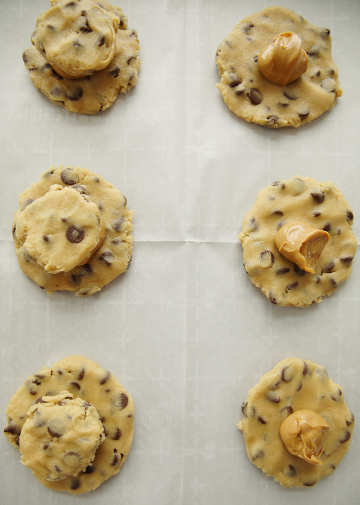 A process photo for peanut butter stuffed chocolate chip cookies. You can see flat rounds of cookie dough laid out on parchment with mounds of peanut butter on all of them and a second small round of cookie dough on top of the peanut butter on some of the photos.