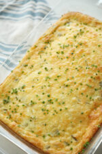 A glass casserole dish with a beautiful chile relleno breakfast casserole sits on a table next to a blue and white dish towel.