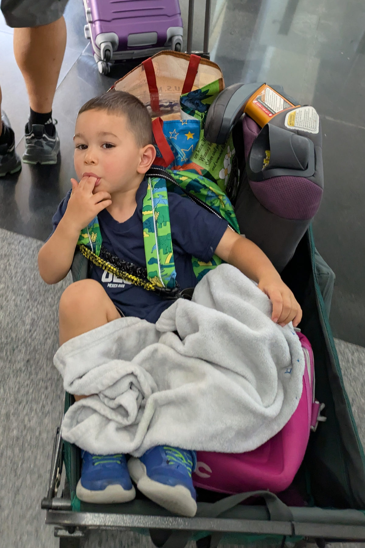 A toddler in the airport in a wagon. 