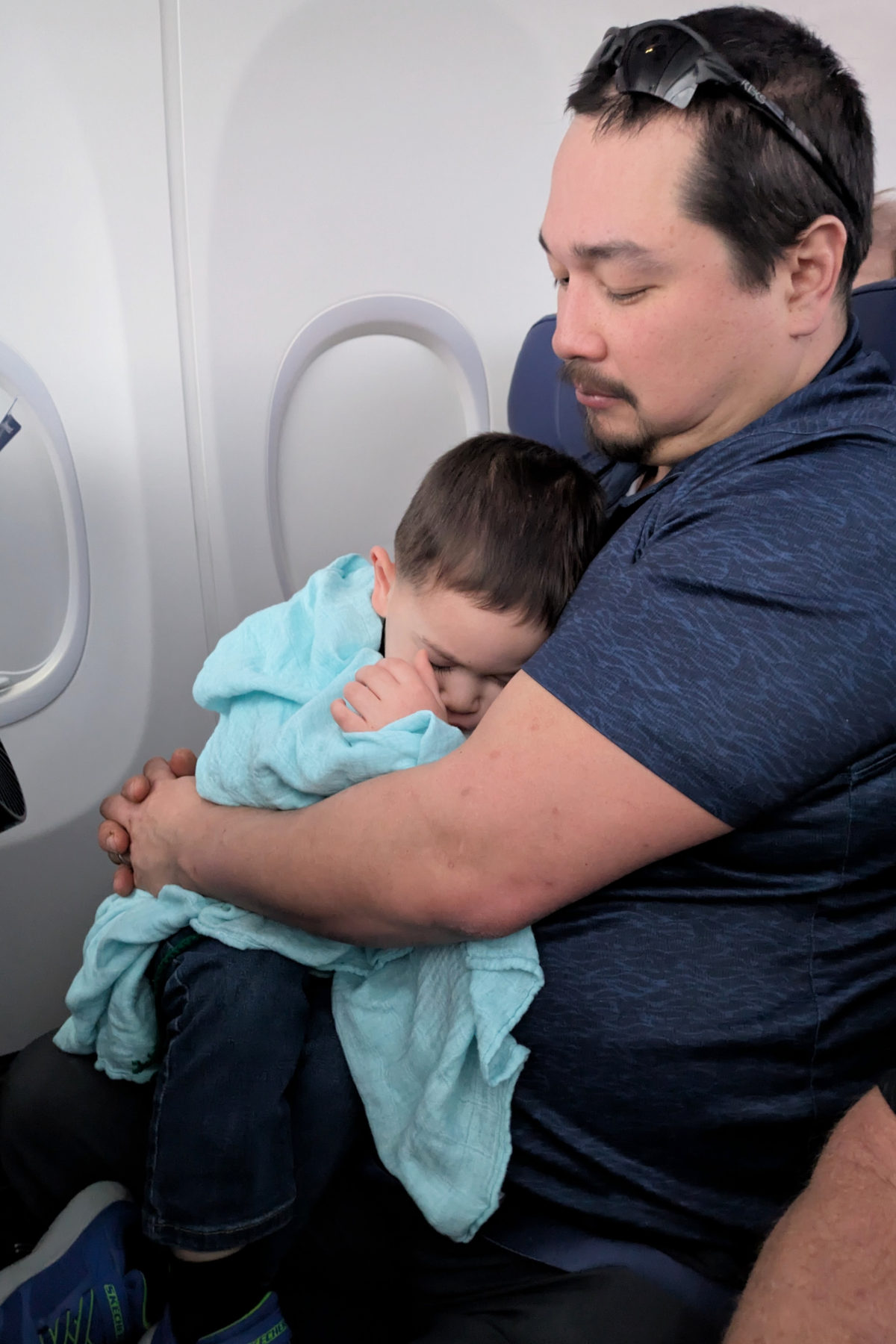 Toddler sleeping on Dad's lap on the airplane. 