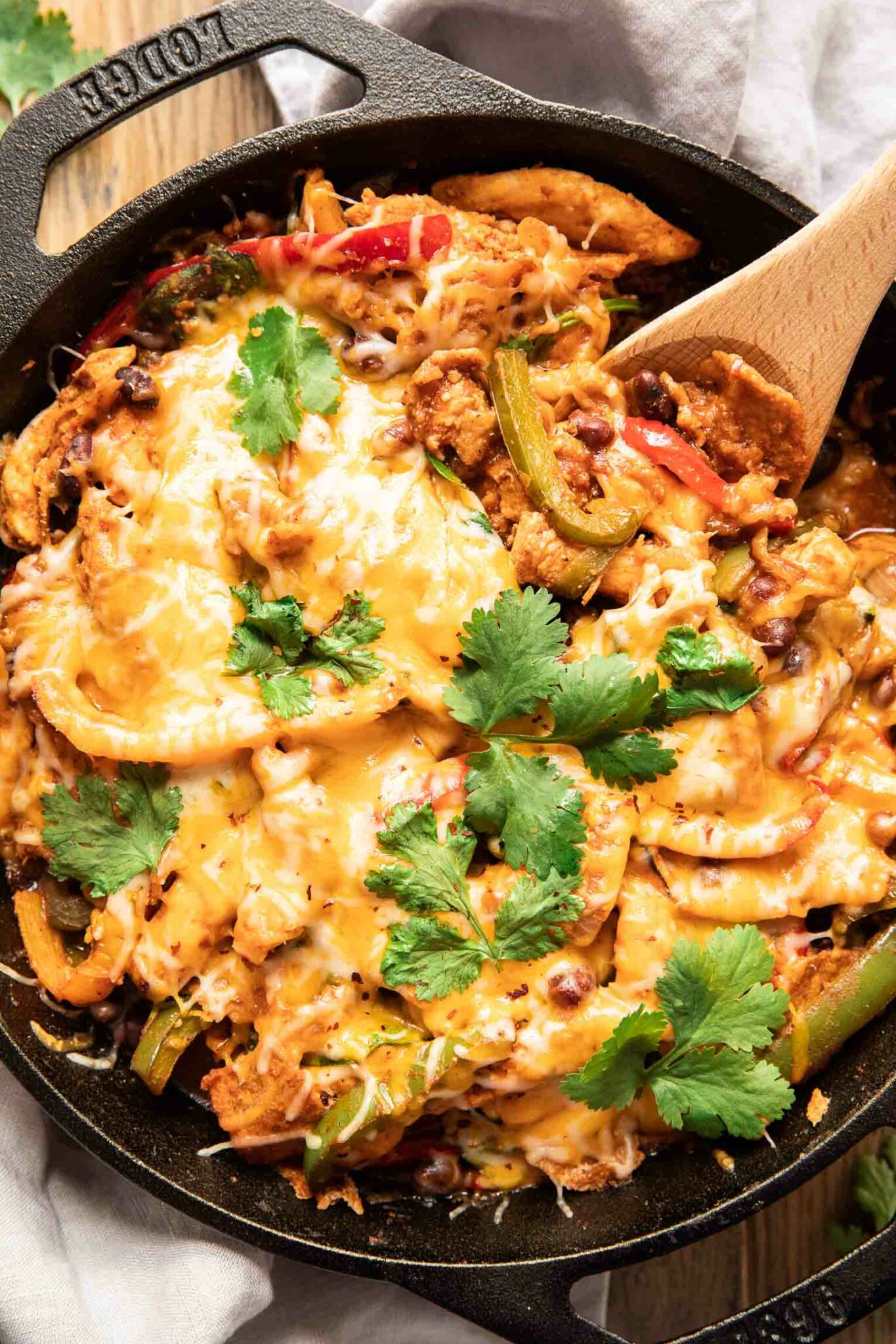 A photo of a chicken fajita casserole in a cast iron pan. It is very cheesy and features fresh cilantro. 