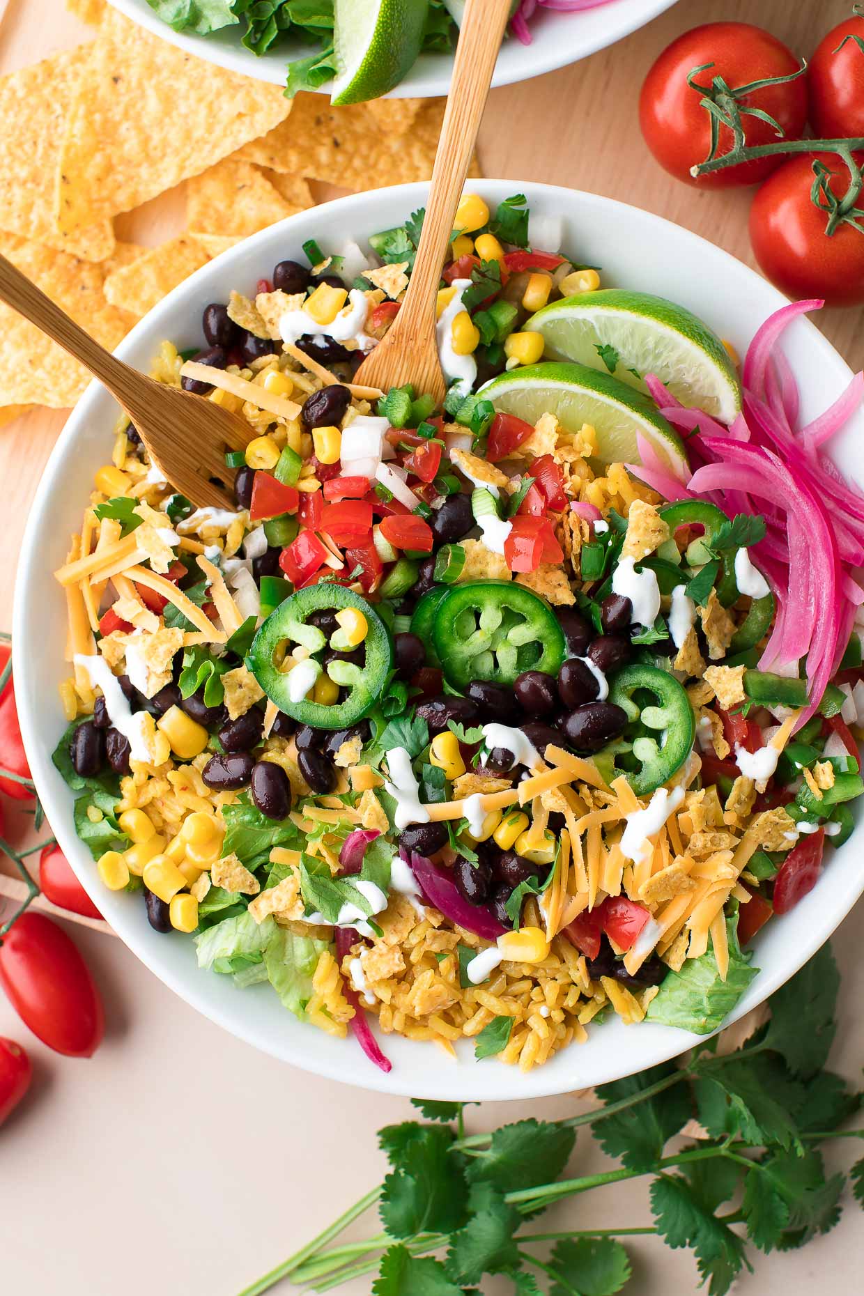 A black bean burrito bowl garnished with pickled onions and jalapeno peppers and wedges of lime.