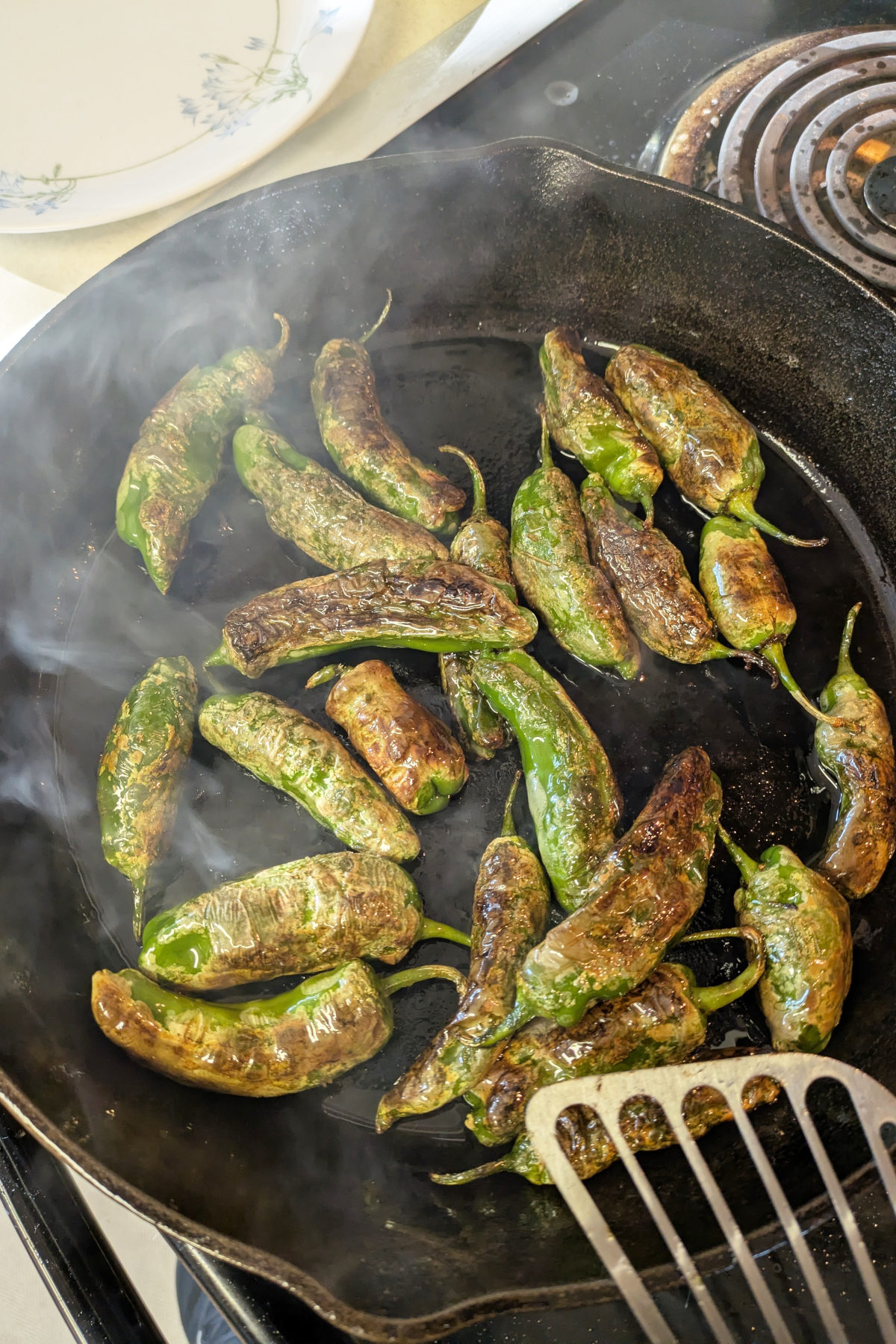 This is a behind the scenes image of blistered shishito peppers cooking in a cast iron skillet preparing for a photo shoot.