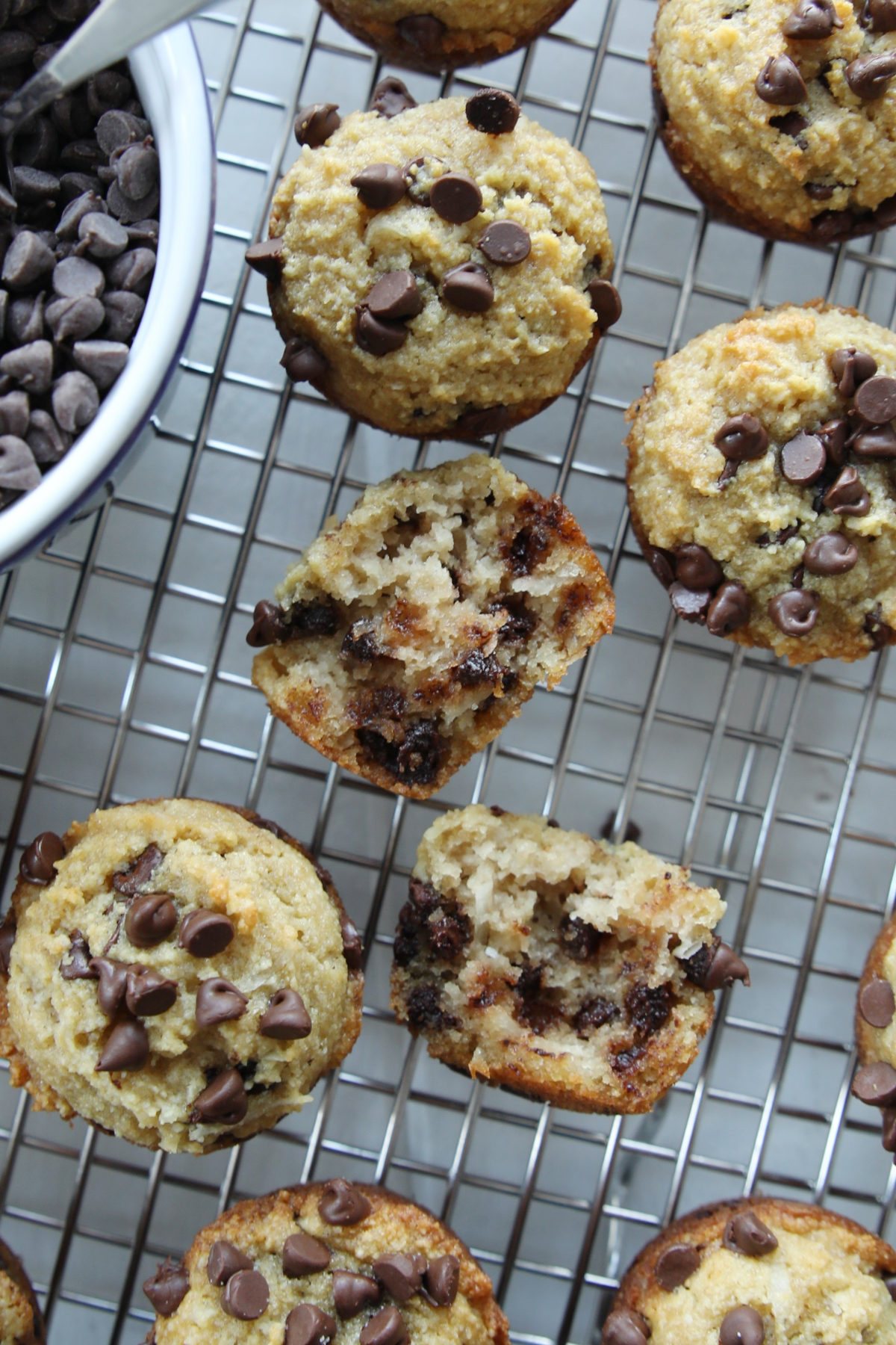mini chocolate chip protein muffins on a metal rack ready to be served. One is split in half so you can see the tender texture inside.