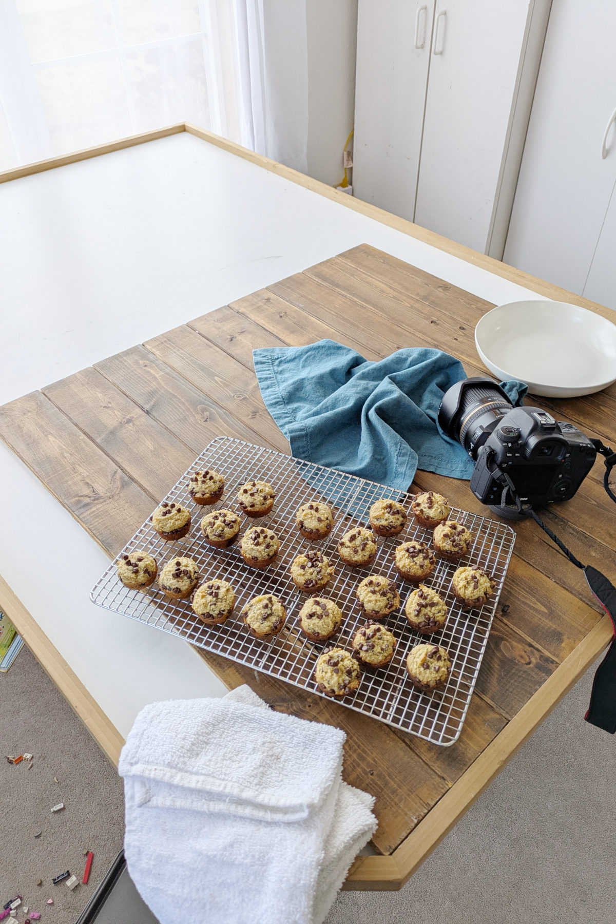 mini chocolate chip protein muffins in the photography studio. They are on a wooden backdrop with a camera, a napkin and a plate. 
