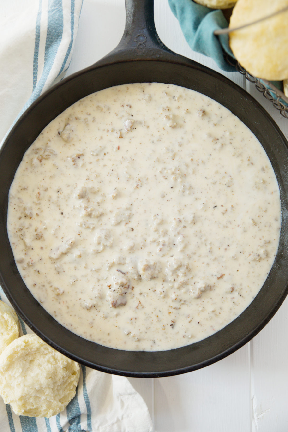 a cast iron pan of sausage gravy sits on a table with some biscuits ready for biscuits and gravy