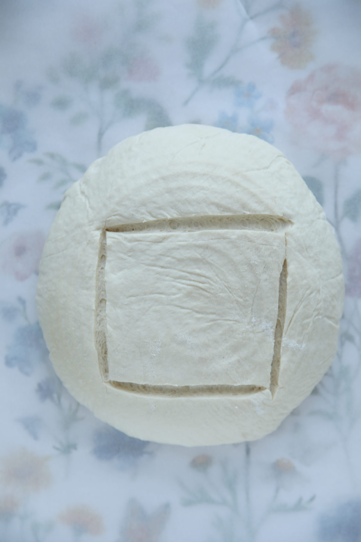 Top-down view of an unbaked sourdough boule with a square box score that shows slightly uneven lines due to low surface tension.