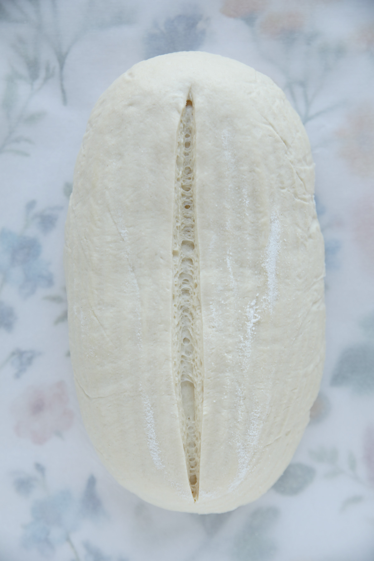 Top-down view of an unbaked sourdough batard with a single, deep vertical score down the center.