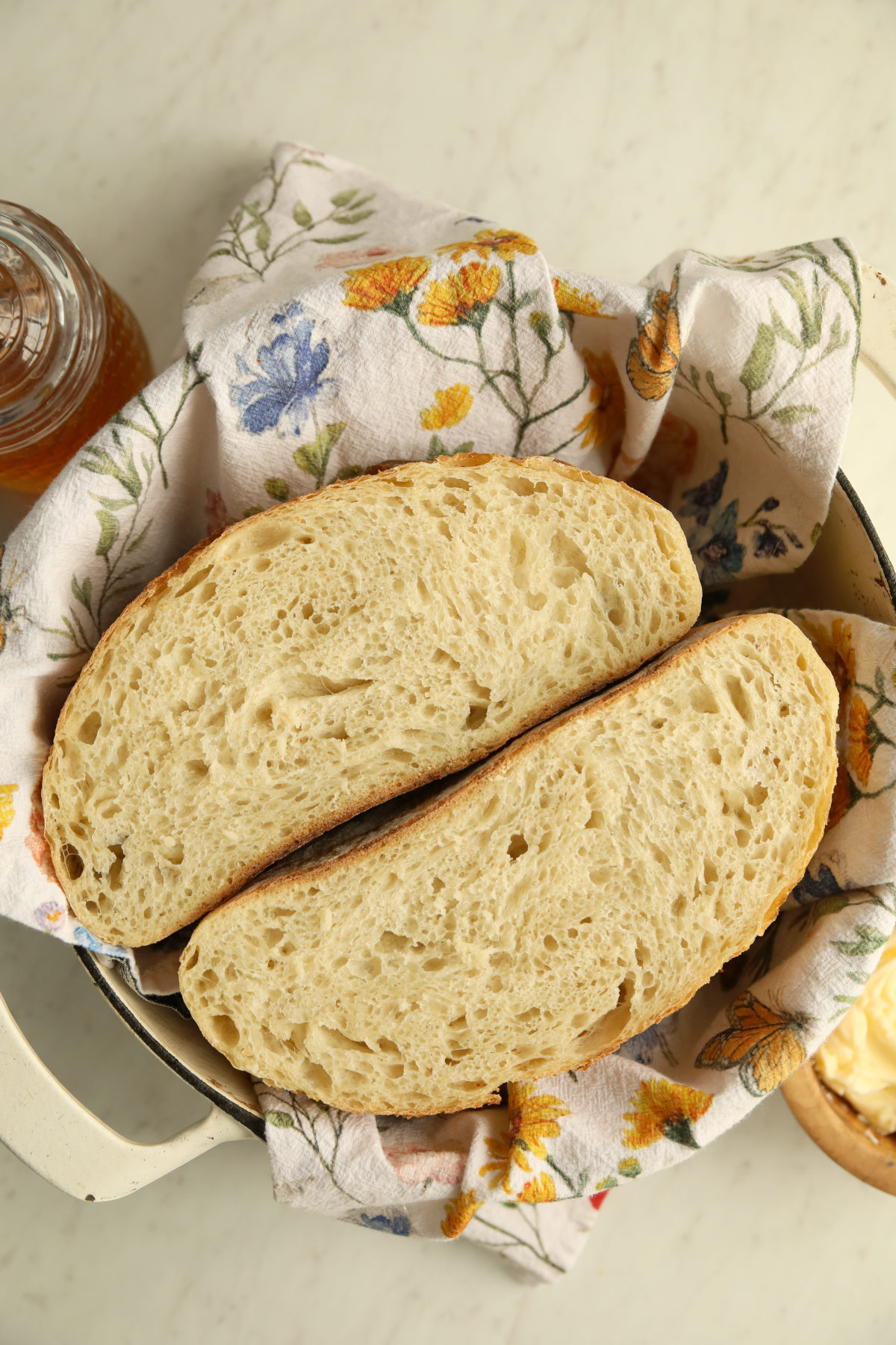 A loaf of sourdough cut in half and tucked into a Dutch Oven with a floral tea towel.