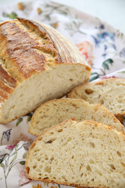 Freshly baked sourdough bread loaf sliced on a floral cloth, showing a golden crust and soft, airy crumb.