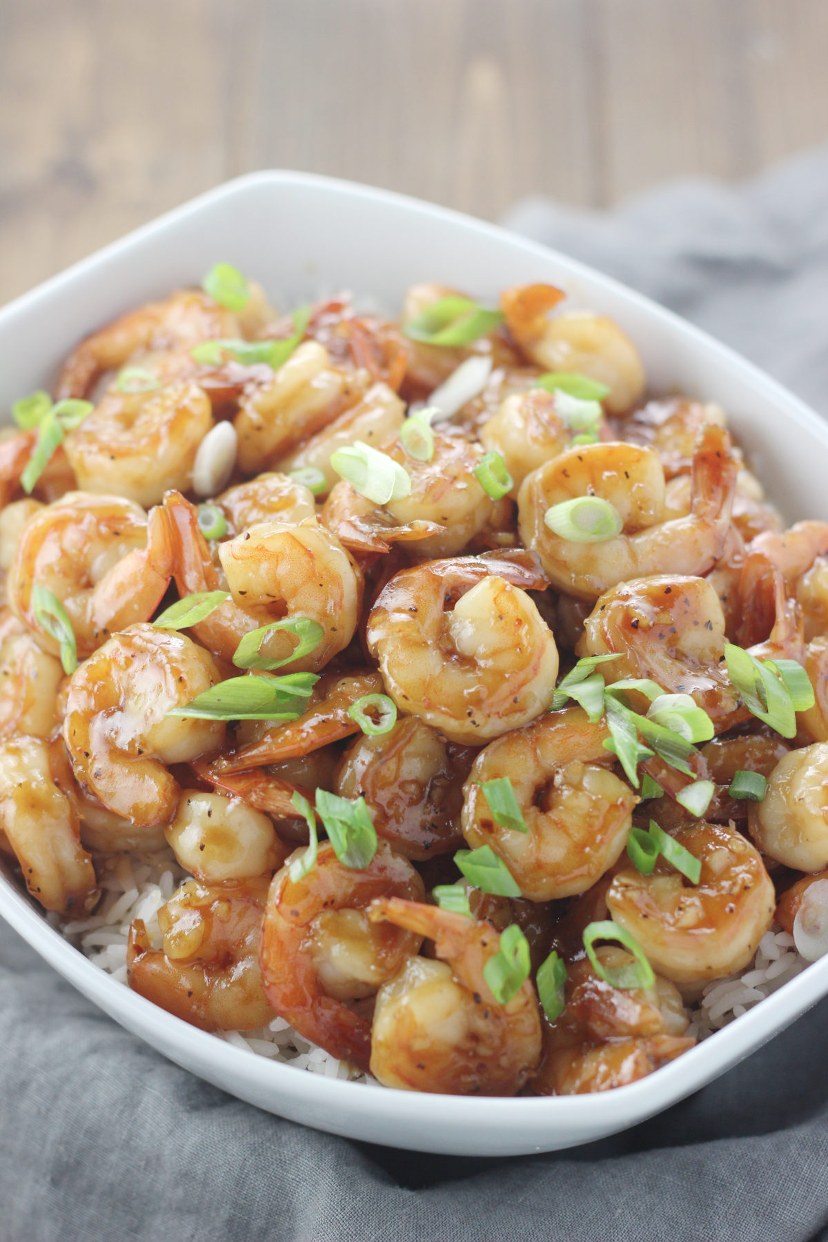 Beautiful shrimp in a glossy honey garlic sauce sit on a bed of white rice. You can see green onion on the shirmp. 