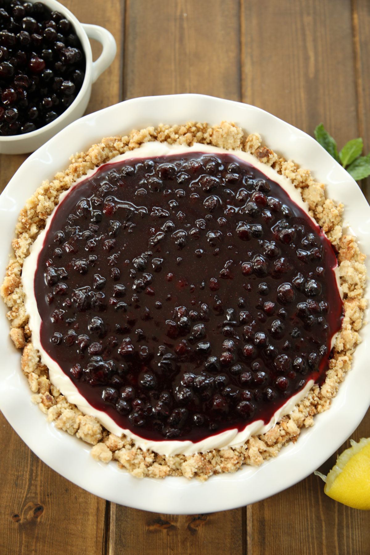A round huckleberry cheesecake is in a white pie plate. You can see a thick layer of fresh huckleberry topping on top of the cheesecake.