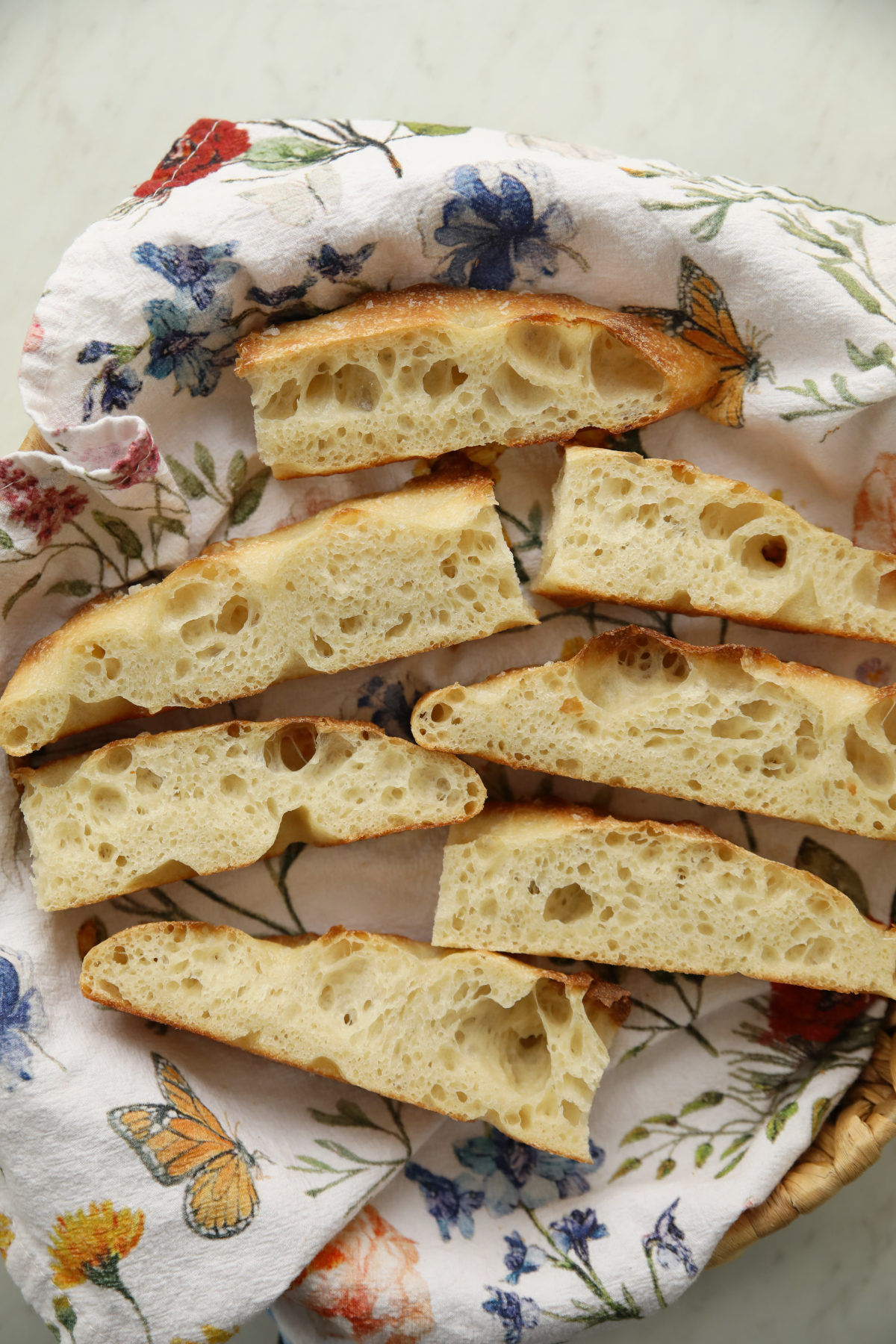 Fresh, bubbly slices of sourdough focaccia bread laid out on a floral tea towel. 