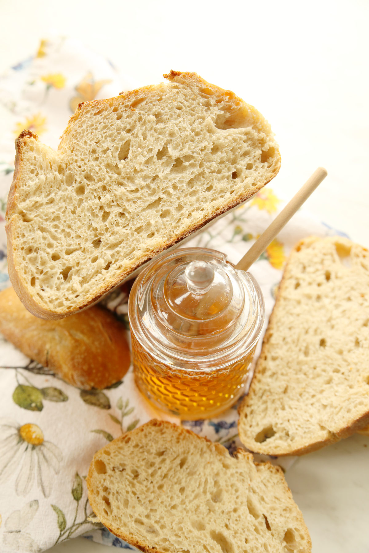 A beautiful boule of artisan sourdough bread for beginners.  The loaf is propped up on a honey pot with other slices around it. 