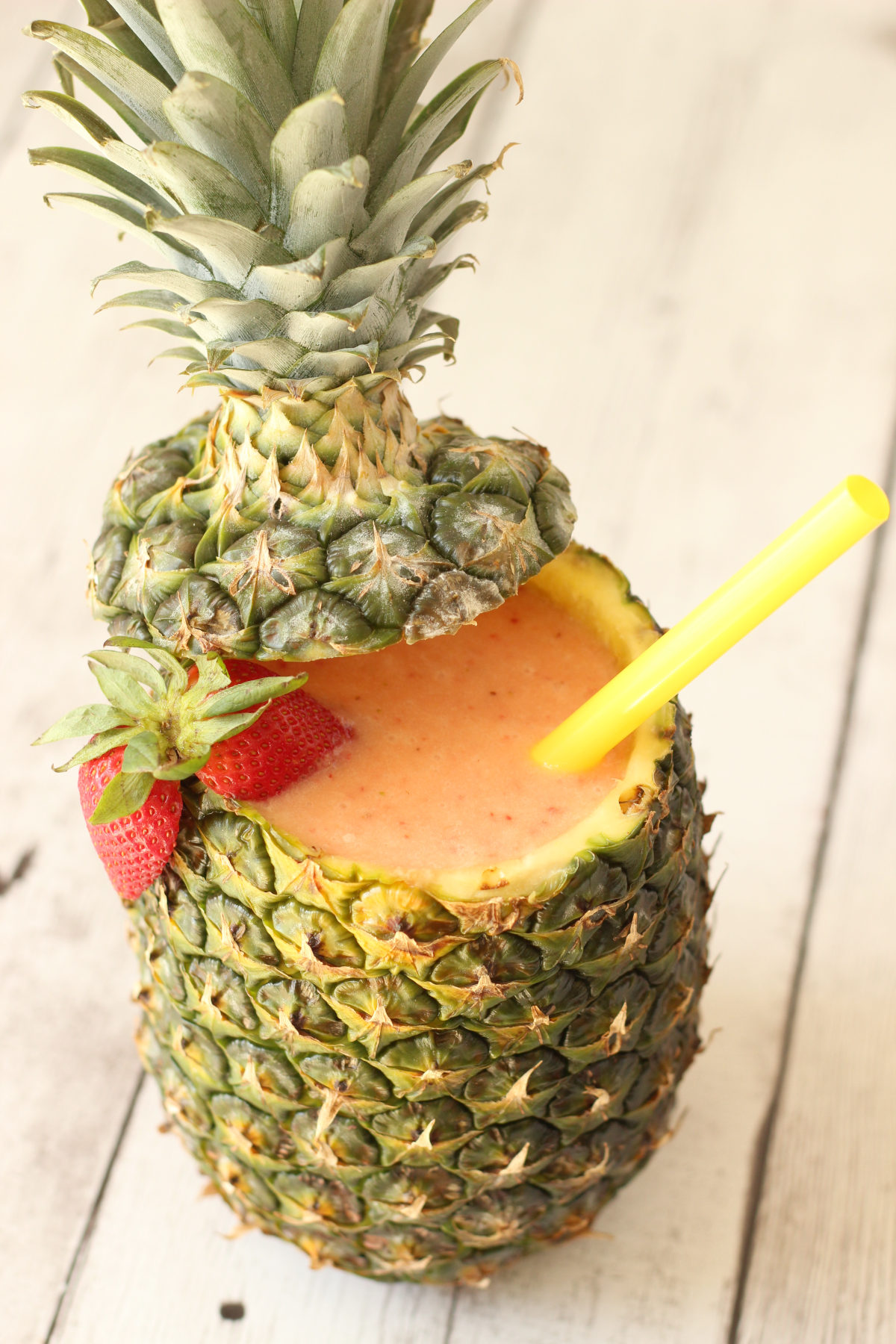 Strawberry pina colada served inside a fresh hollowed pineapple with a yellow straw and strawberry garnish