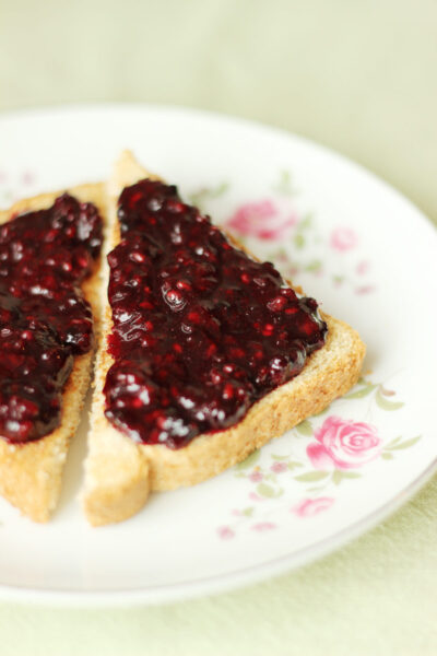 Homemade low sugar blackberry jam spread over whole wheat toast triangles on a white rose china plate sitting on a green table cloth.