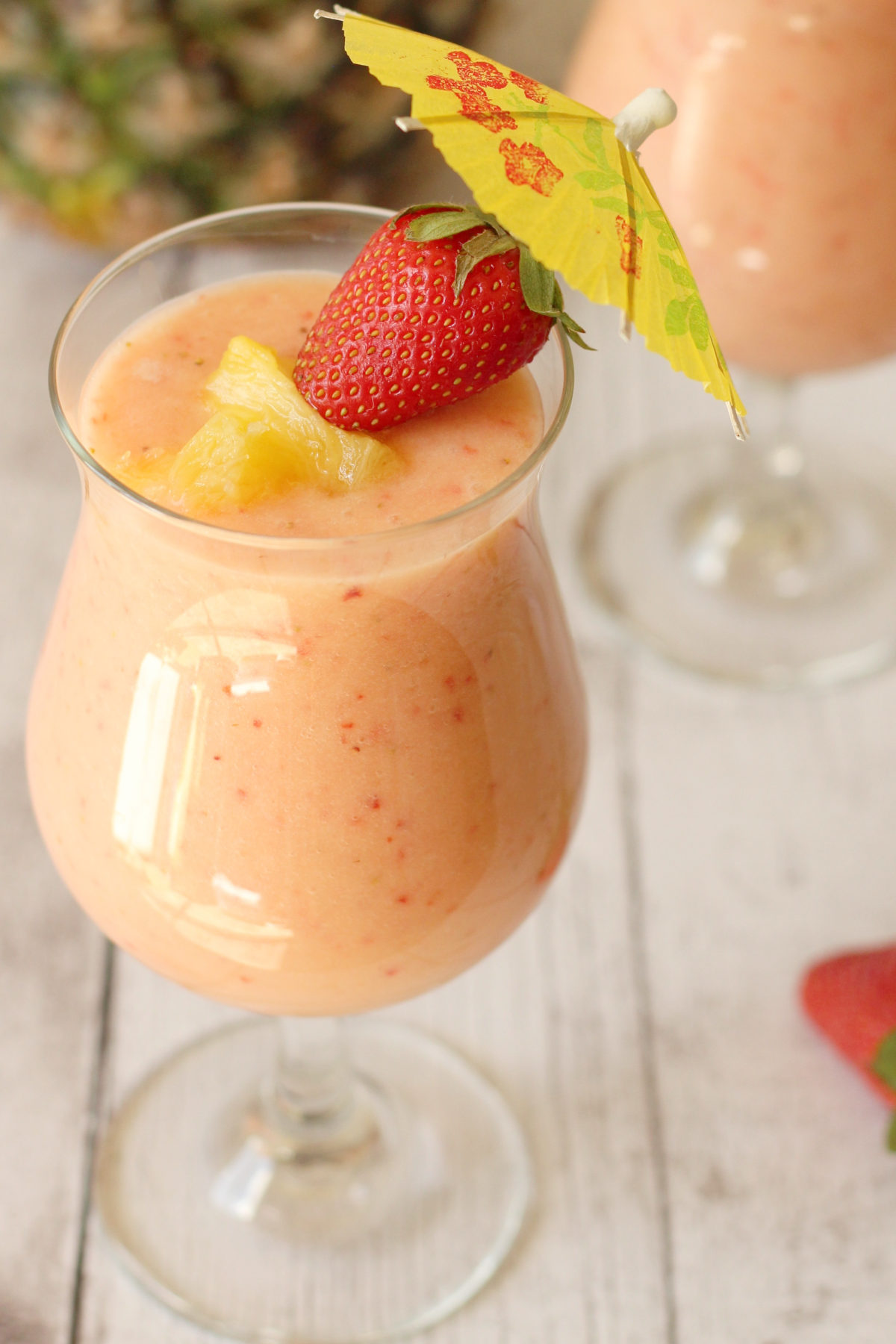 A stemmed glass filled with creamy strawberry pina colada, garnished with a fresh strawberry, pineapple chunks, and a tropical cocktail umbrella