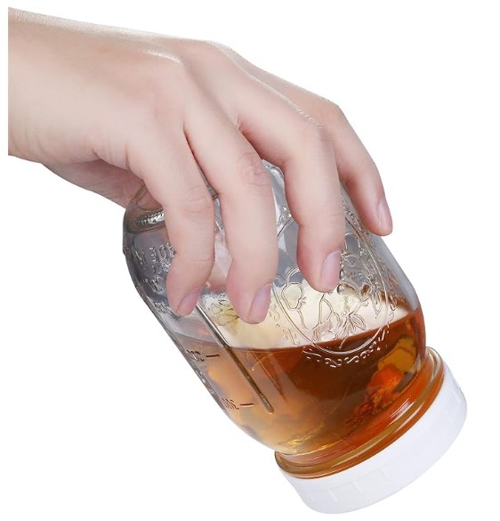 a hand holds a mason jar with a white lid. The jar has liquid and is upside down.