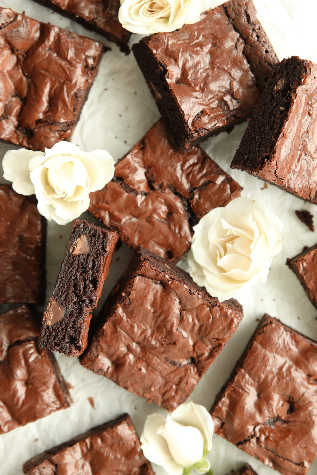 Close up of fudgy sourdough discard brownies with a shiny crinkled top, one brownie propped to show the dense chocolatey interior with visible chocolate chips.